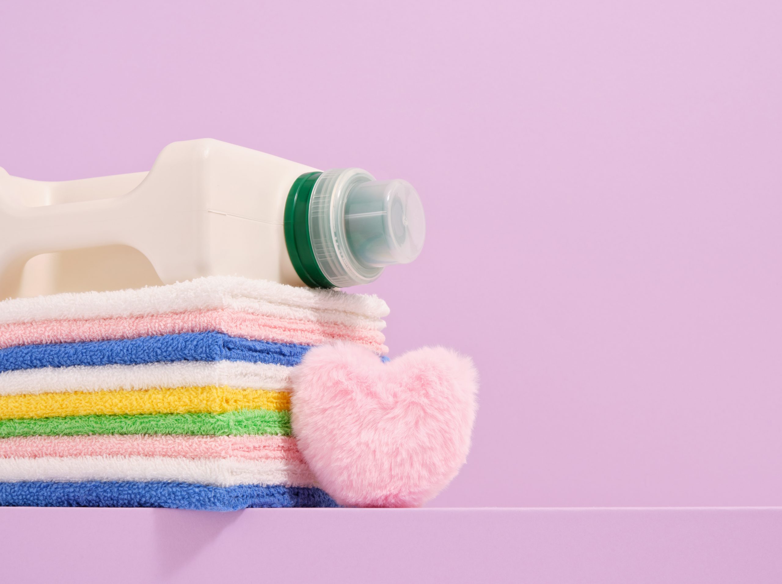 Detergent bottle, colorful towels and pink soft heart. Copy space for text.